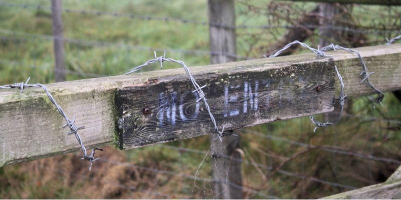 A fence covered in barbed wire with a faded "no entry" painted on it. 